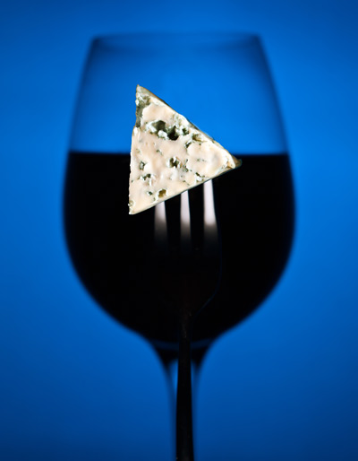 Piece of Stilton in teh shape of a Play icon, on a folk. Infront a glass of Port.